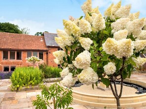 A brick building with a circular stone garden featuring white flowering plants. - Cottage With En-suite Bedrooms (Exeter)