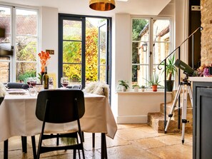 Ein Essbereich mit Tisch für zwei Personen, einem auf einem Stativ montierten Teleskop und Blick auf einen Garten durch große Fenster.