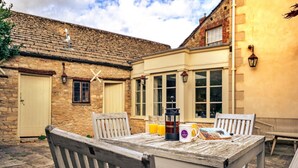 An outdoor patio with a wooden table and chairs, a coffee maker, and a mug. - Cotswolds Manor With Garden (Lechlade)