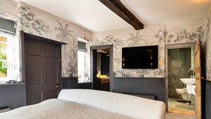 A bedroom with a large bed, a television mounted on the wall, and a bathroom visible through an open door. - Cotswolds Manor With Garden (Lechlade)