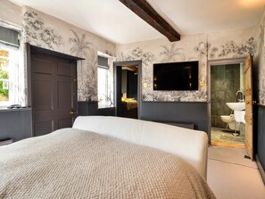 Ein Schlafzimmer mit einem großen Bett, einem an der Wand montierten Fernseher und einem durch eine geöffnete Tür einsehbaren Badezimmer.
