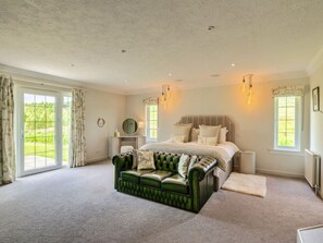A bedroom with a large bed, a green sofa, and a view of the outdoors through a sliding door. - Luxury Country Estate Near Largs (Largs)