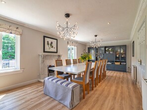 A dining area with a white table, wooden chairs, a bench, a fireplace, and a chandelier. - Luxury Country Estate Near Largs (Largs)