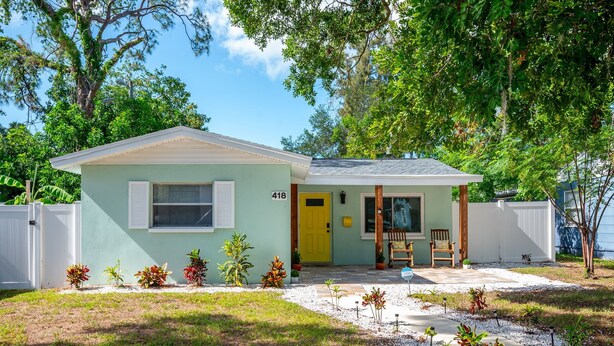 A single-story house with a front porch, a number '418' sign, and a small garden with various plants. - Lemon Door Cottage (St. Petersburg)