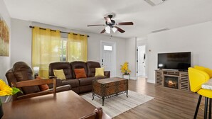 A living room with a sofa, coffee table, TV, fireplace, and a dining area with chairs and a table. - Lemon Door Cottage (St. Petersburg)