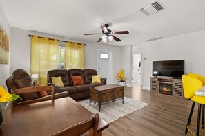 Ein Wohnzimmer mit Sofa, Couchtisch, Fernseher, Kamin und einem Essbereich mit Stühlen und Tisch.