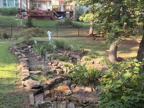 Un jardín con un sendero de piedra, un pequeño estanque y una terraza de madera.