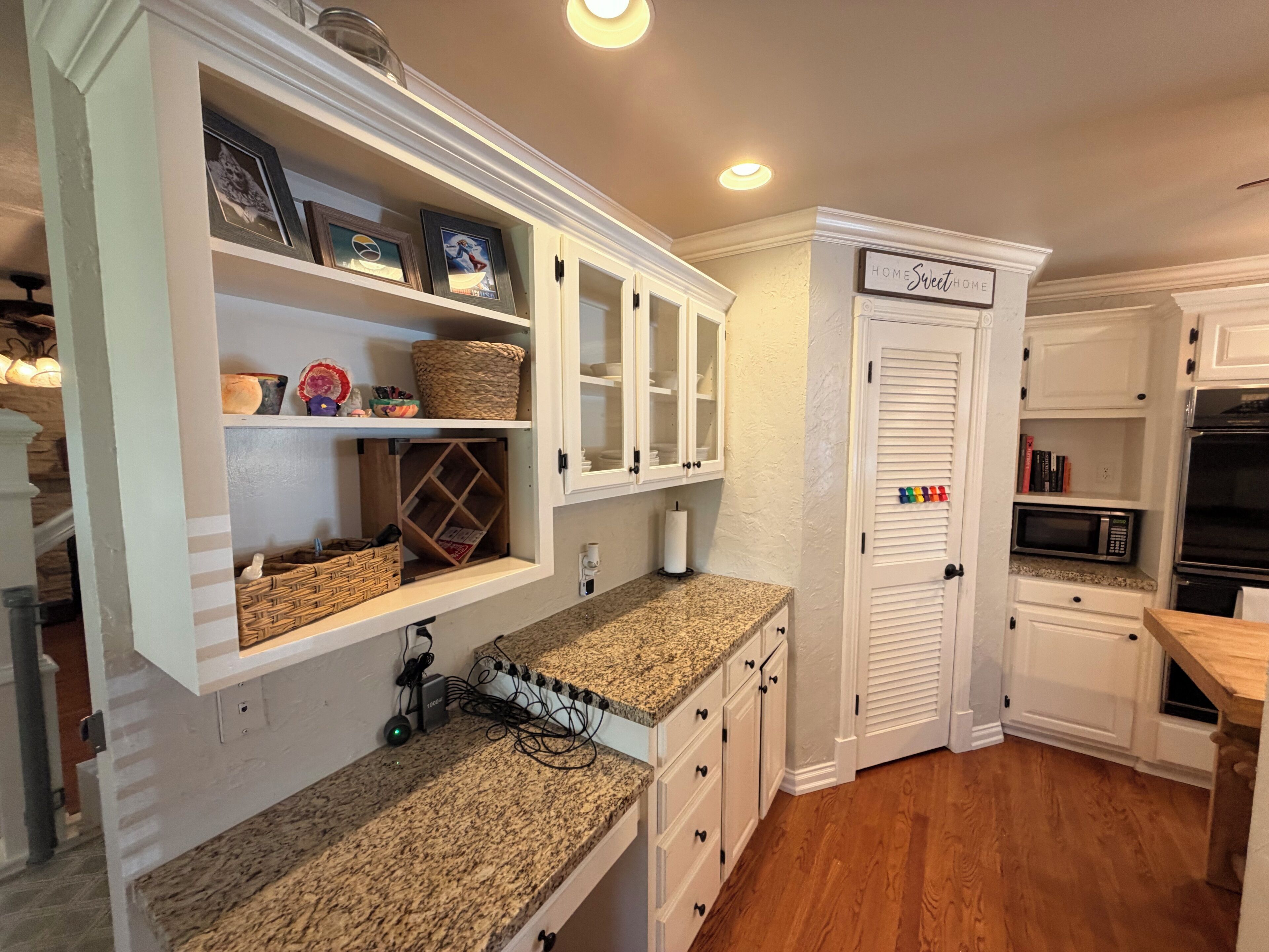 A kitchen with white cabinetry, a granite countertop, and a sign that reads 'HOME Sweet HOME'.