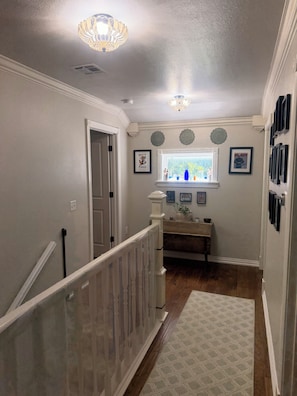 A hallway with a staircase, a window with decorative molding, and a wall with framed pictures.
