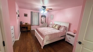 Ein zartrosa eingerichtetes Schlafzimmer mit Bett, Nachttischen, Schreibtisch und Deckenventilator.