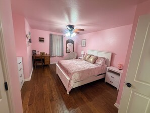 Ein zartrosa eingerichtetes Schlafzimmer mit Bett, Nachttischen, Schreibtisch und Deckenventilator.