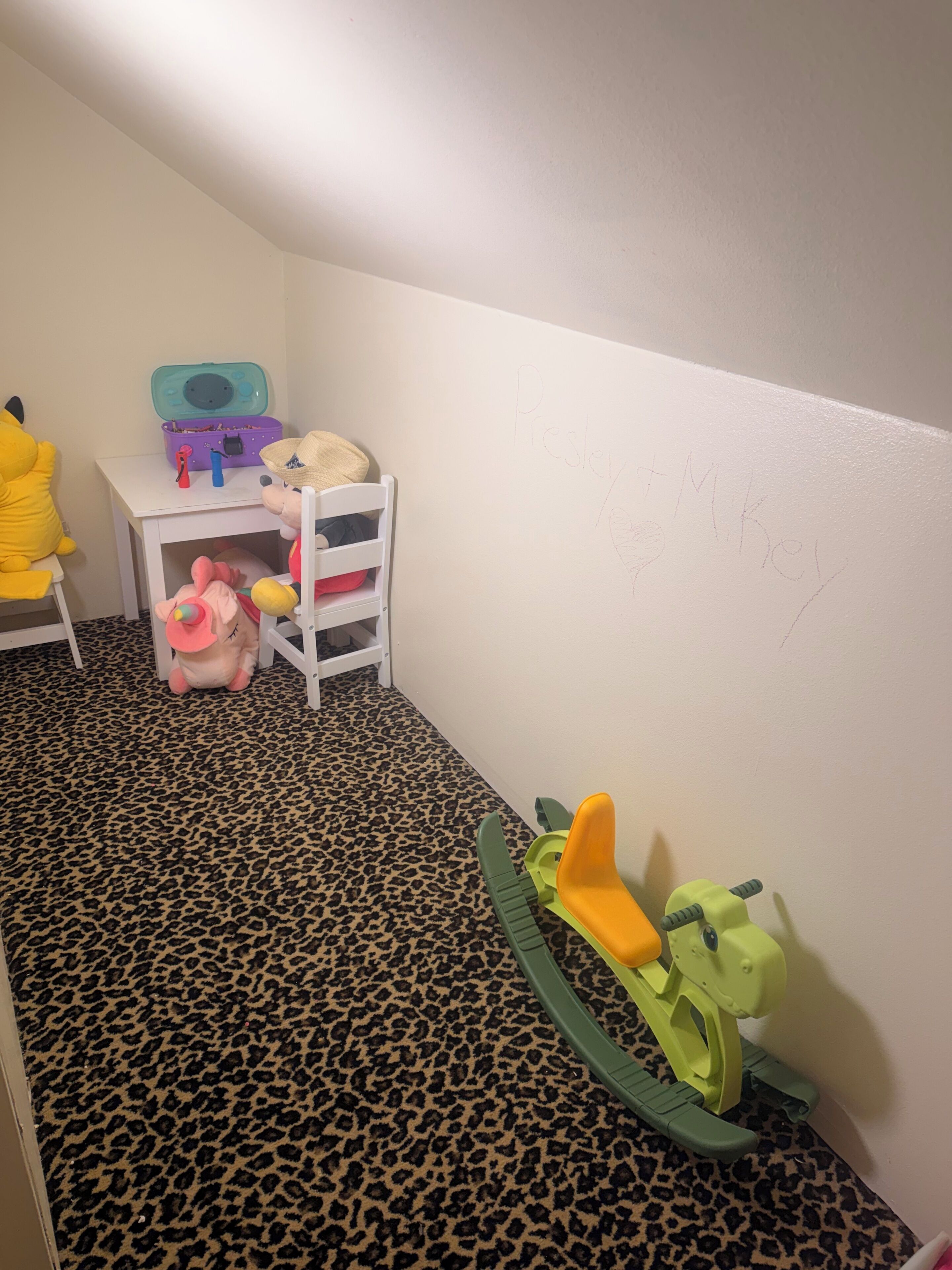 Un espace de jeux pour enfants avec une chaise blanche, une petite table avec des jouets et un tapis à motifs léopard.