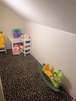 A child's play area with a white chair, a small table with toys, and a leopard print carpet.