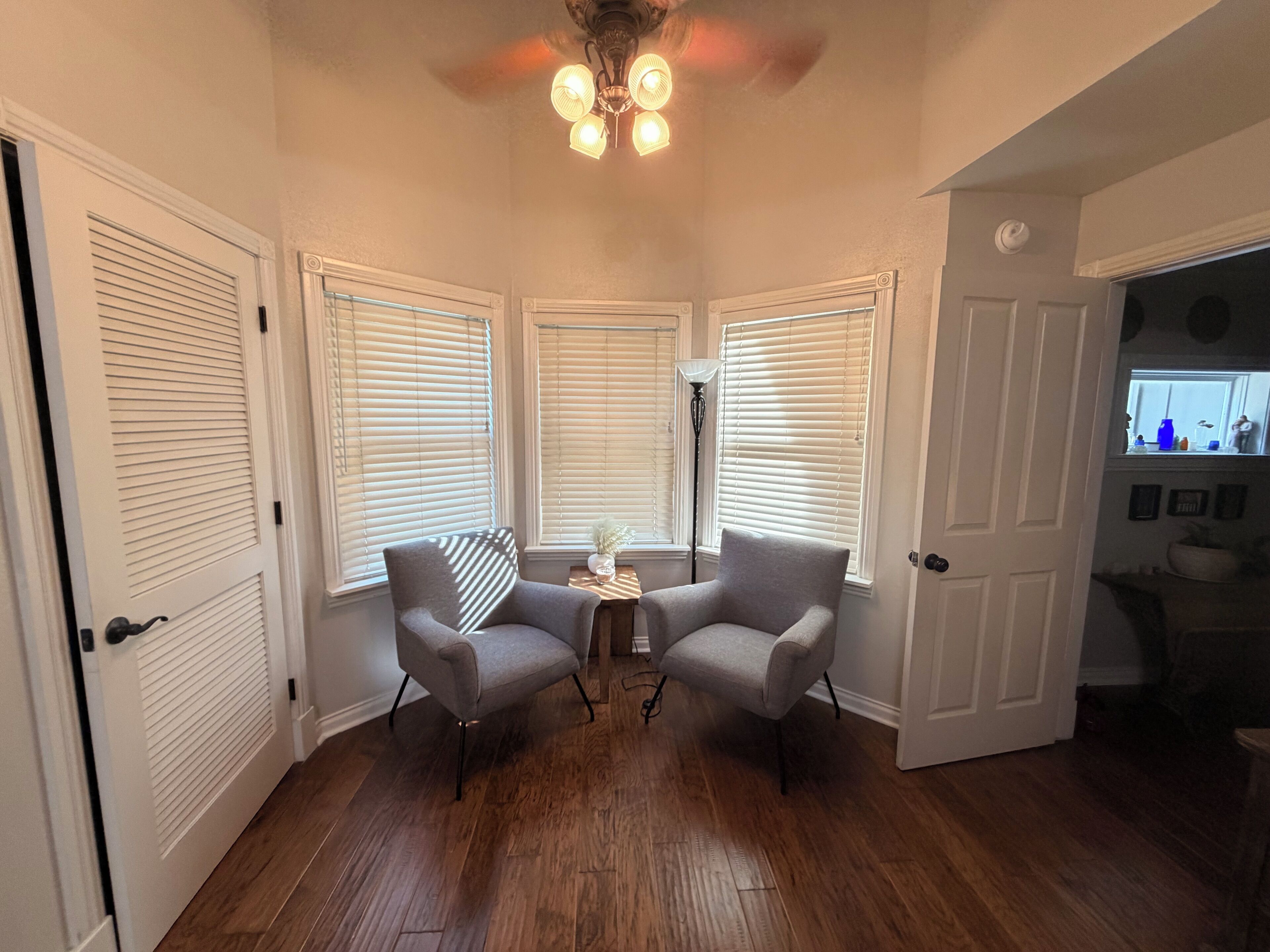 A room with a corner seating area, a ceiling fan, and a window with blinds.