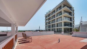A rooftop terrace with a seating area, a building with multiple balconies, and a clear sky. - Modern Oasis 2BR Condo/ Walk to Camarones Beach & Malecón (Puerto Vallarta)