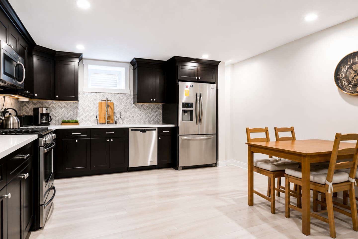 Una cocina moderna con armarios oscuros, electrodomésticos de acero inoxidable y una mesa de comedor de madera con sillas.