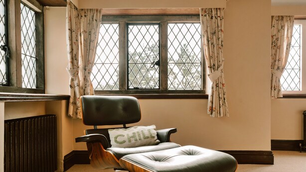 Ein Zimmer mit einem einzelnen schwarzen Ledersessel, einem Heizkörper und einem Fenster mit blumigen Vorhängen.