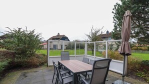 A covered patio area with a table and chairs, a metal umbrella, and a view of a house and garden. - Detached Dune Villa With Hot-tub (Makkum)