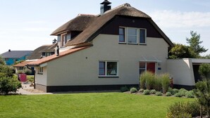 A two-story house with a thatched roof, a brick exterior, and a well-maintained lawn. - Detached Dune Villa With Hot-tub (Makkum)