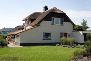 Ein zweistöckiges Haus mit Strohdach, Ziegelaußenwand und einem gepflegten Rasen.