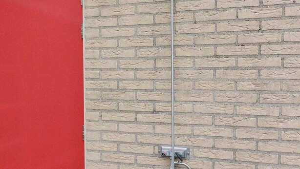 A brick wall with a metal pipe extending vertically, a red door, and a small metal box with a hose attached. - Detached Dune Villa With Hot-tub (Makkum)