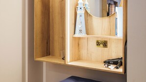 A wooden vanity with a mirror, a small shelf with a lighthouse model, and a blue ottoman. - The Boat Inn (Oughterard)