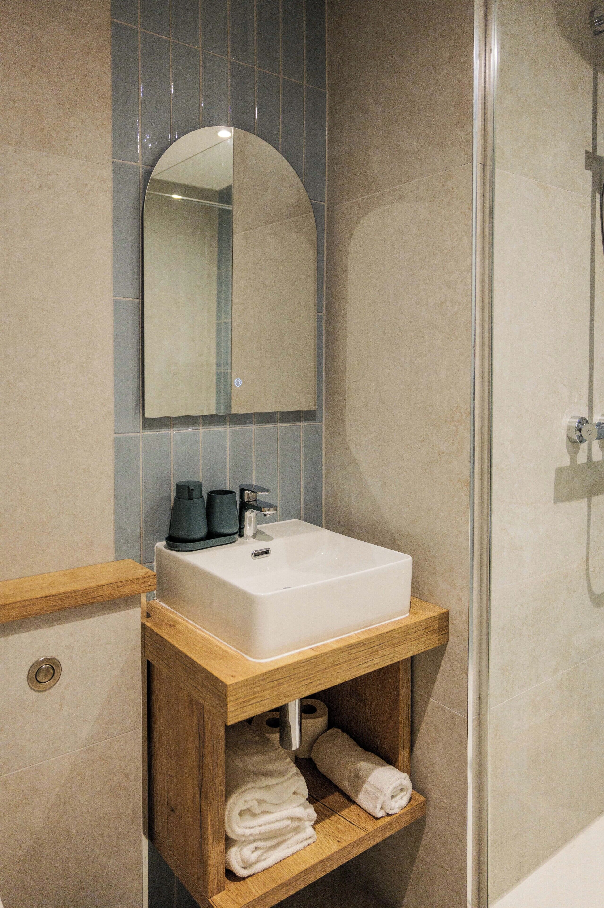 A bathroom with a white sink, a mirror, and a wooden shelf with towels.