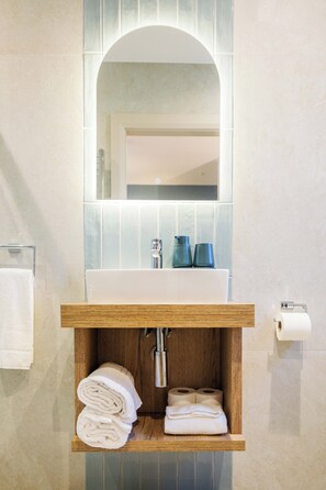 A bathroom with a wooden vanity, a sink, a mirror, and a shelf with towels.