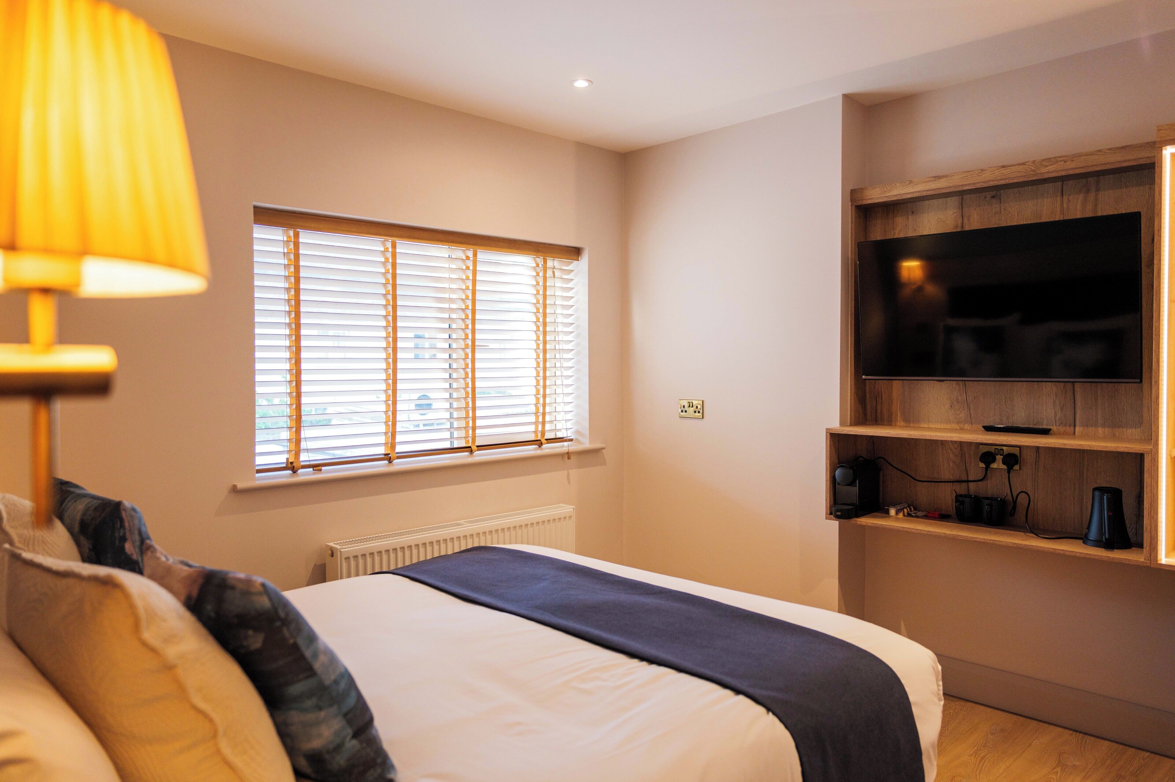 Een hotelkamer met een bed, een raam met zonwering, een televisie bevestigd aan een houten plank en een radiator.