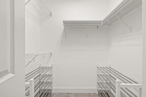 Ein begehbarer Kleiderschrank mit weißen Wänden, Metallregalen und Holzboden.