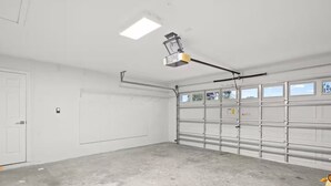 En garage med betongulv, en hvid dør og en garageport med vinduer.