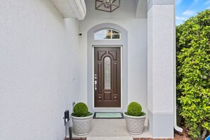 Ein Haus mit einer braunen Tür, weißen Wänden und zwei in Töpfen stehenden Formschnitten auf der Veranda.