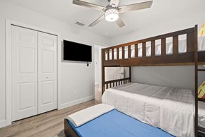 Ein Zimmer mit Etagenbett, Deckenventilator, Fernseher und weißen Türen.