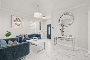 A modern living room with a blue sofa, a white coffee table, and a round mirror on the wall. - Modern Boutique House/Heated Pool/Clearwater/Tampa (Tampa)