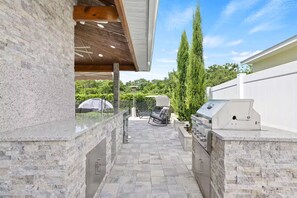 Eine Terrasse im Freien mit einer Steinarbeitsplatte, einem Grill und einer Sitzecke mit Tisch und Stühlen.