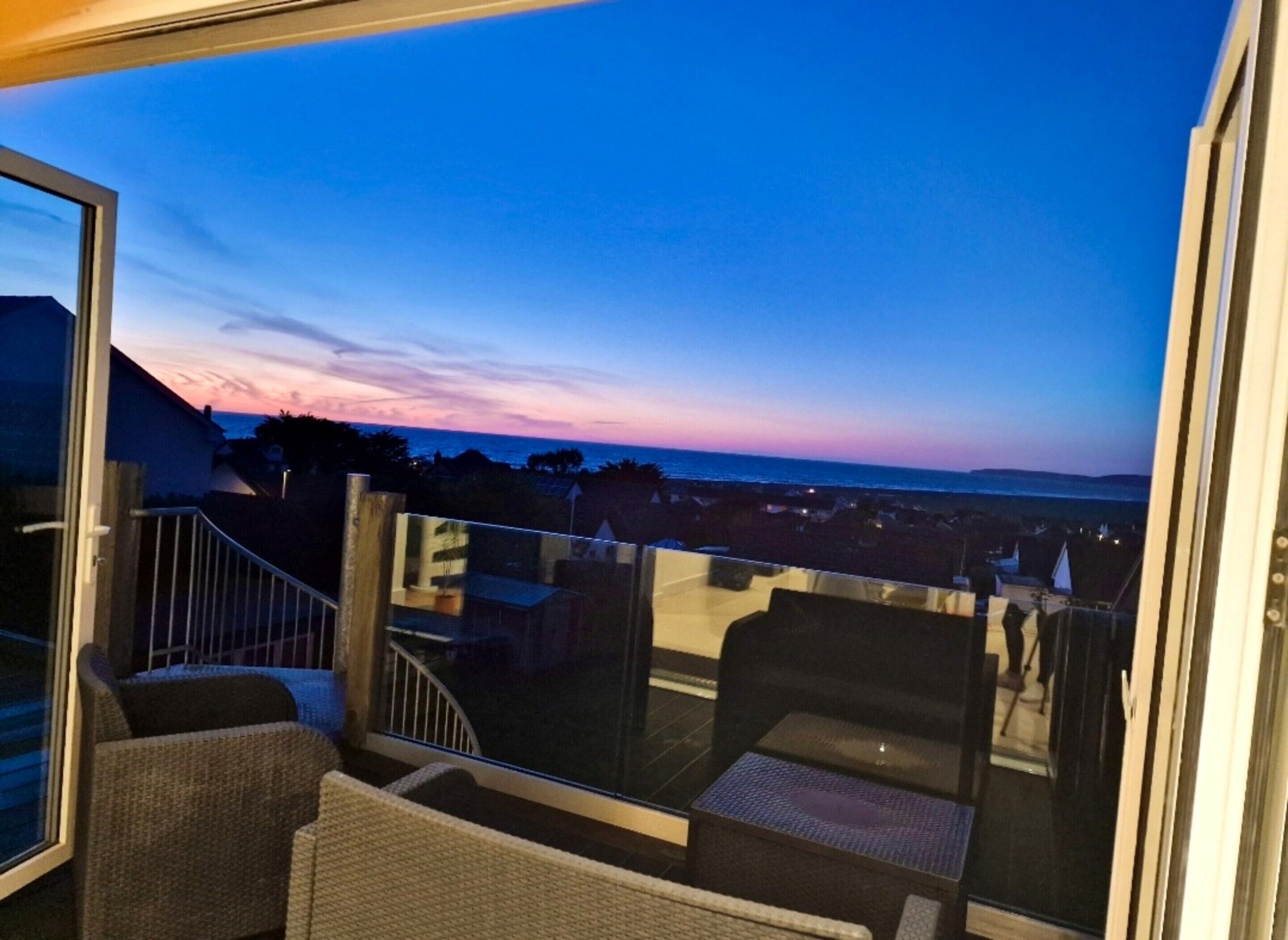 A balcony with outdoor seating and a view of the sea at dusk.