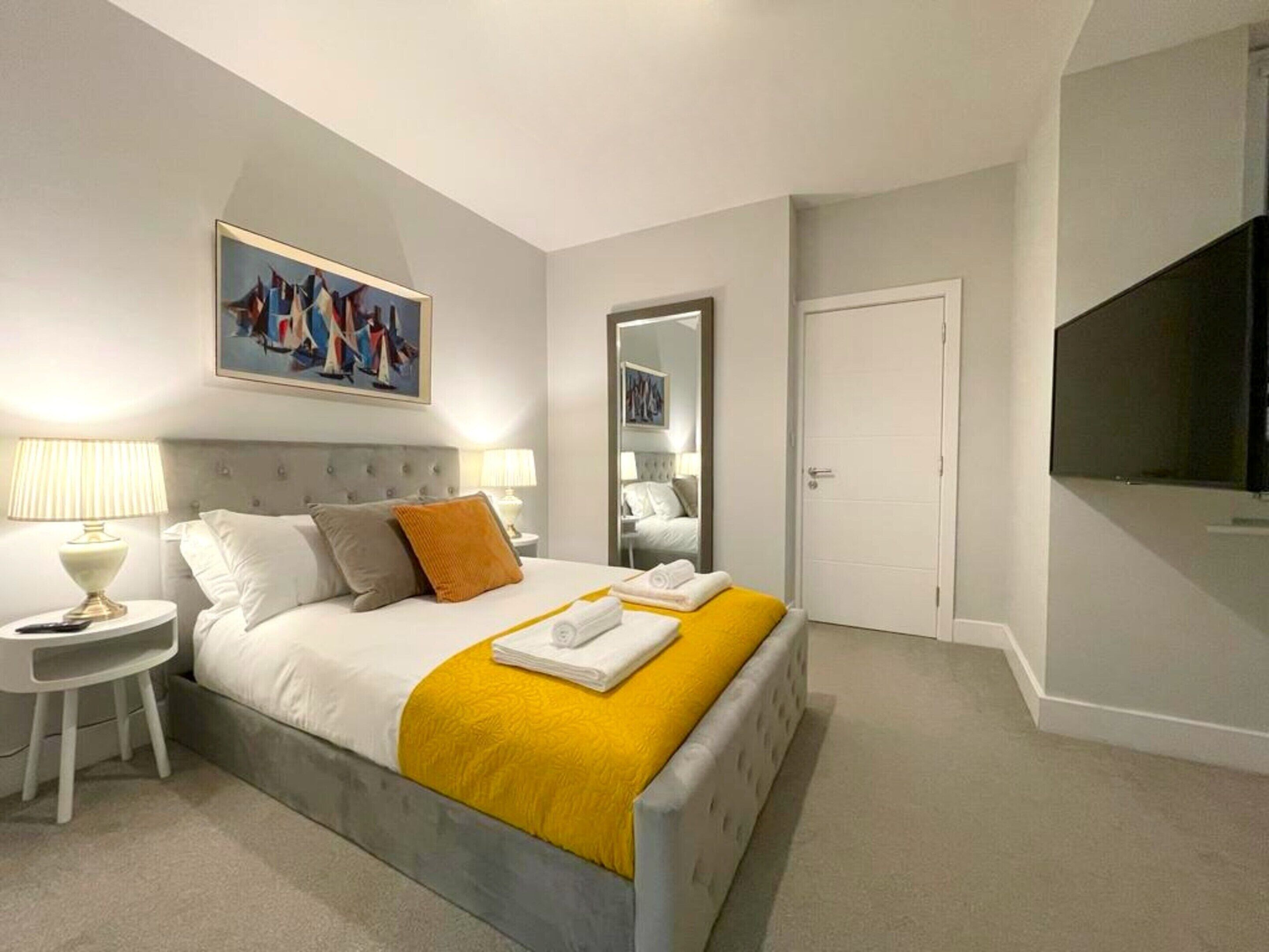 A hotel room with a bed, two bedside tables, a painting, a wardrobe, and a television.