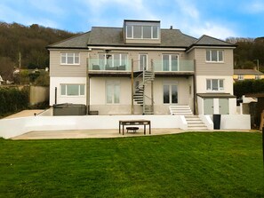 A two-story house with a front staircase, a small patio, and a grassy yard. - Lush Beach House With hot tub Access (Bideford)