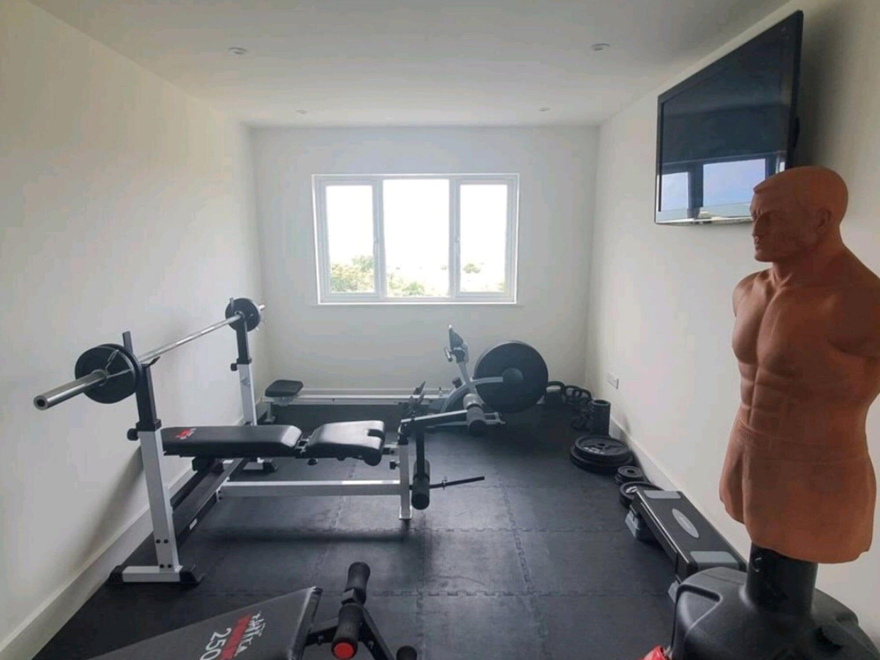 Ein Fitnessraum mit Trainingsgeräten, einer Bank und einem großen Fenster.