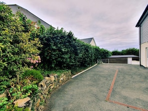 A paved driveway leading to a garage, flanked by dense shrubbery and a stone wall. - Lush Beach House With hot tub Access (Bideford)