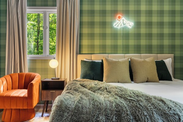 Ein Schlafzimmer mit Bett, Nachttisch, Lampe, Stuhl und einem Fenster mit Vorhängen.