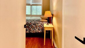 A narrow hallway leading to a bedroom with a bed, a bedside table with a lamp, and a window with blinds. - Spacious 4-bedroom house in gorgeous Houston with AC (Houston)