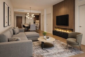 Un salon moderne avec un canapé d’angle, une table basse ronde, une cheminée et un téléviseur à écran plat fixé au mur.