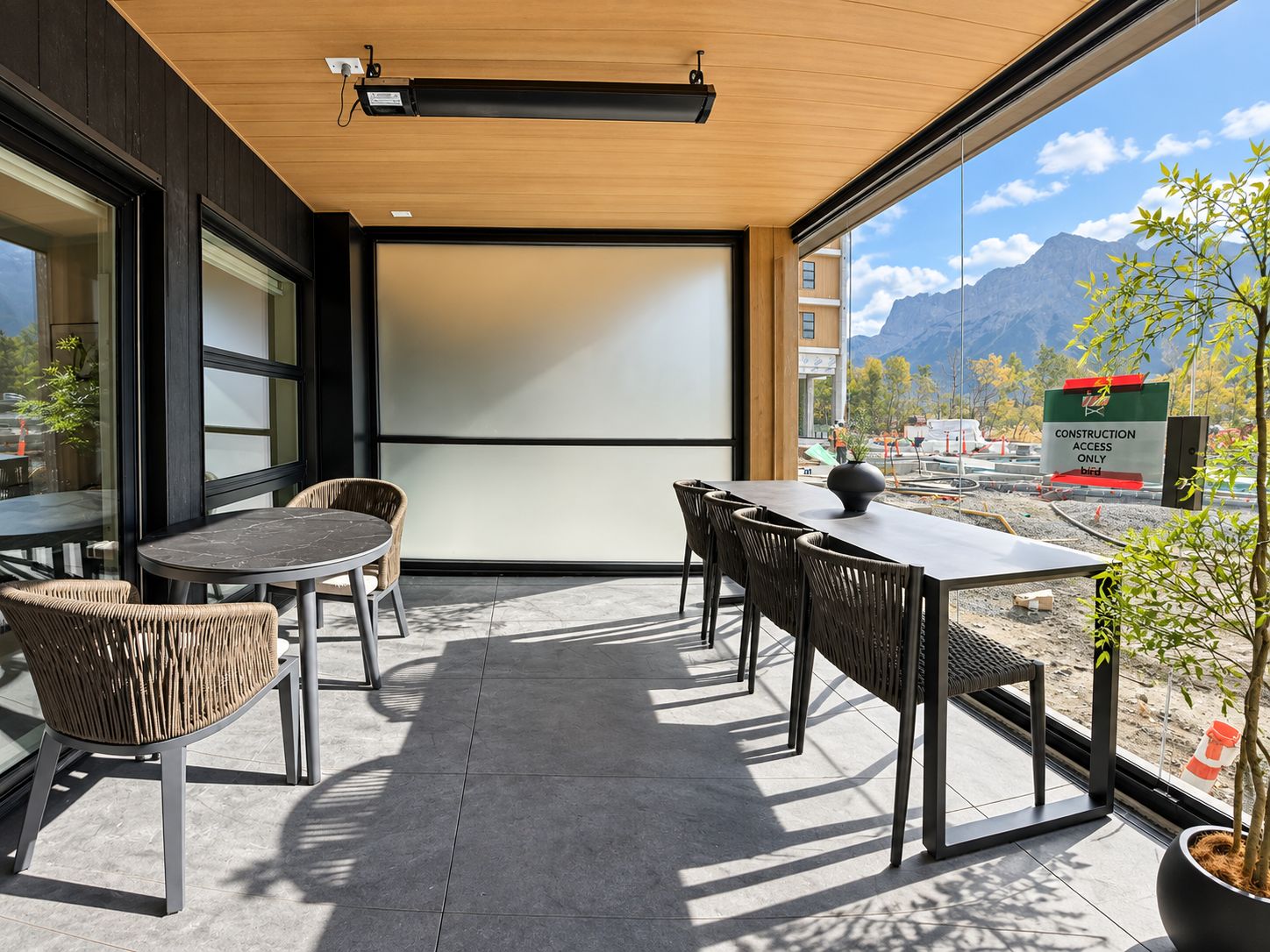 An outdoor seating area with a table and chairs, a projector screen, and a view of a construction site with mountains in the background.