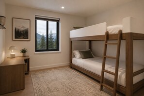 Une chambre avec des lits superposés, un bureau, une fenêtre donnant sur des arbres et des montagnes, et un tableau encadré accroché au mur.