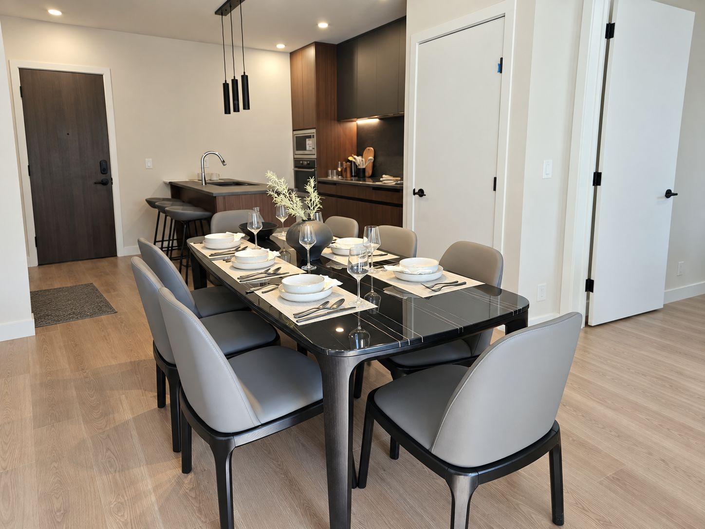 A modern dining area with a black marble table, grey upholstered chairs, and a kitchen in the background.