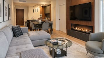 A modern living room with a sectional sofa, a glass coffee table, a fireplace, and a flat-screen TV.