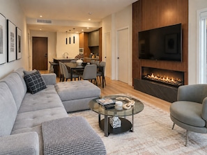 Una sala de estar moderna con un sofá modular, una mesa de centro de vidrio, una chimenea y un televisor de pantalla plana.