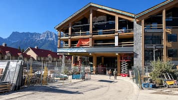 A multi-story building with a wooden facade, a covered entrance, and a view of mountains in the background.