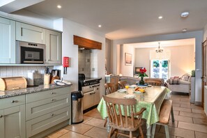 A kitchen with a built-in oven, a stove, and a dining area with a table set for two. - Exmoor Retreat Near the Harbor (Lynmouth)
